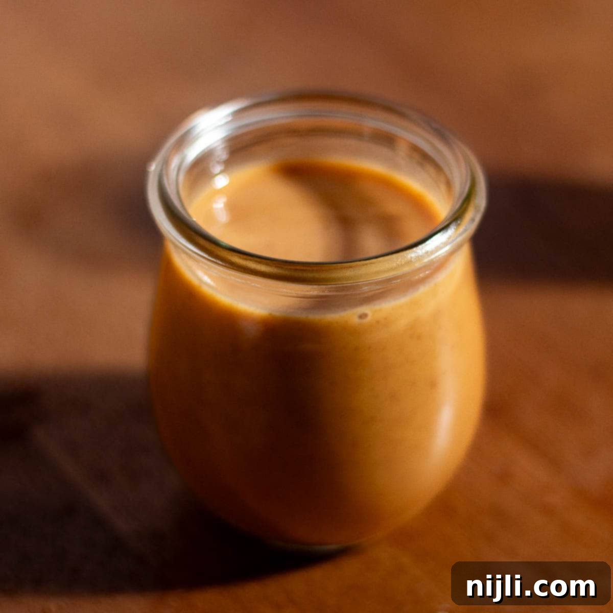 Starbucks Pumpkin Spice Sauce 2 A glass jar filled with copycat Starbucks pumpkin sauce on a wooden counter, ready to be used in homemade coffee drinks.