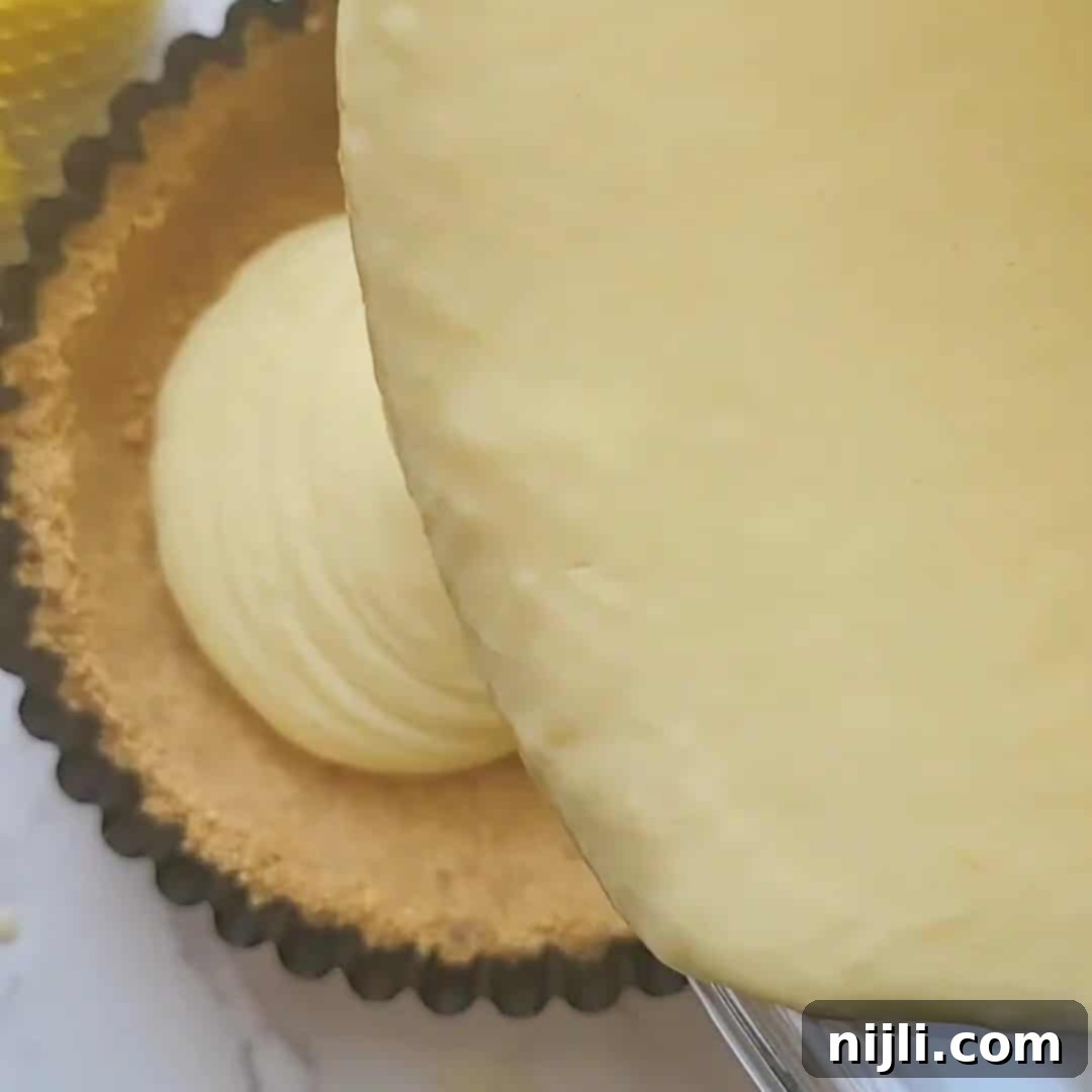 Zesty Lemon Icebox Pie 11 Pouring lemon icebox pie filling into graham cracker crust.