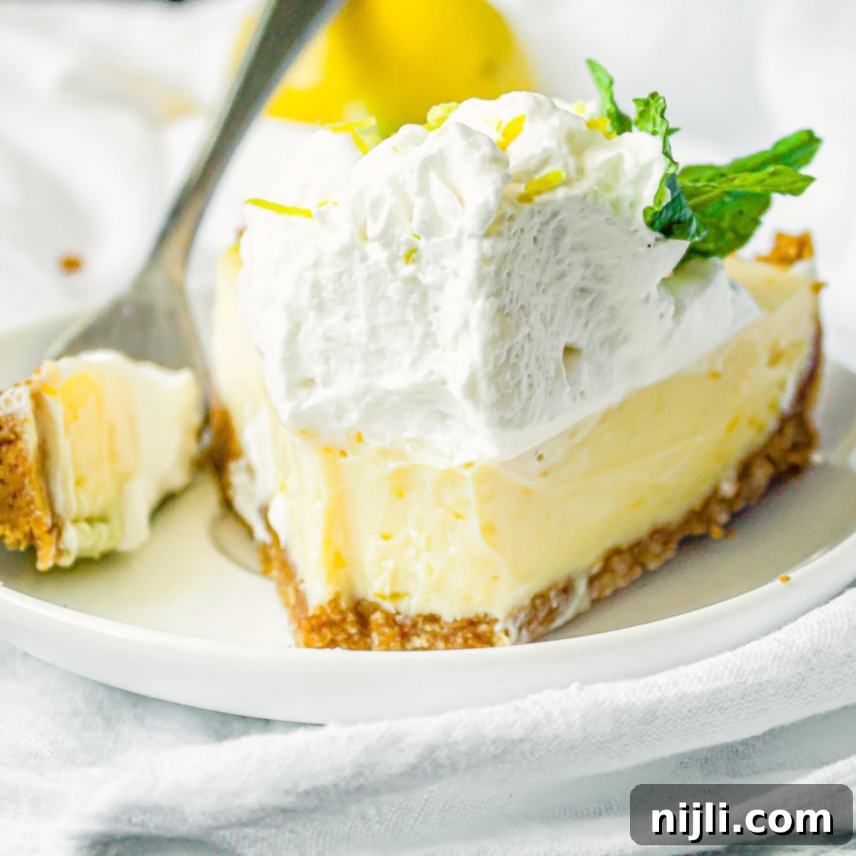 Zesty Lemon Icebox Pie 7 lemon icebox pie on a plate with a bite cut out