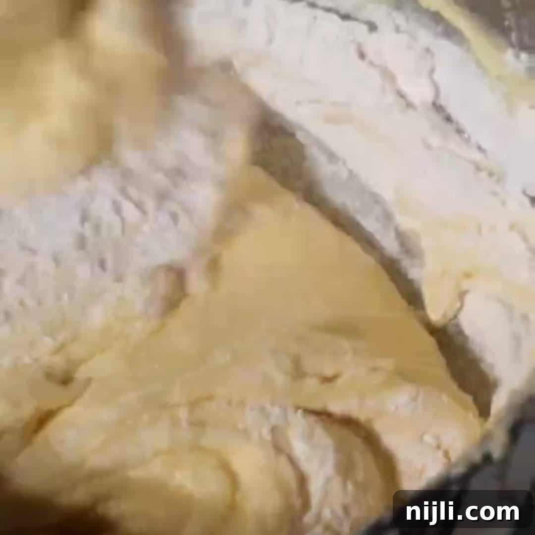 Golden Kentucky Butter Cake with Salted Caramel Glaze 11 the bowl of a stand mixer filled with salted caramel kentucky butter cake batter, with a spatula folding in flour
