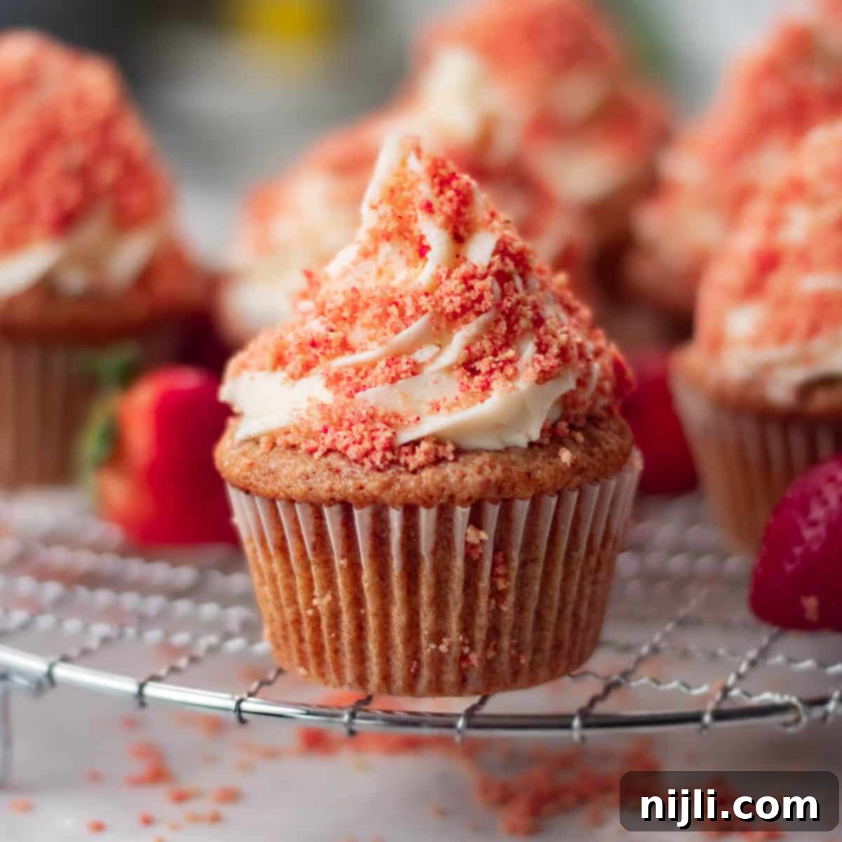 Strawberry Crunch Cupcakes 2 Gourmet strawberry crunch cupcakes with a delightful strawberry topping, set against a blurred kitchen background.