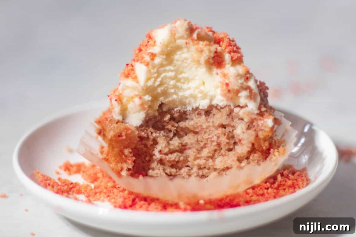 Strawberry Crunch Cupcakes 14 Close-up of a half-eaten strawberry crunch cupcake revealing its moist texture, with crumbs scattered on a white plate.