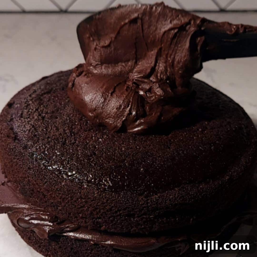 Matilda's Decadent Chocolate Cake 13 The final step of applying a thick, shiny layer of chocolate fudge frosting onto a cooled chocolate cake, symbolizing the creation of Matilda's Chocolate Cake.