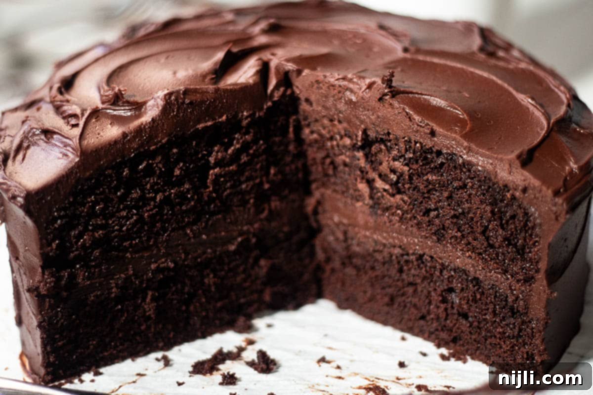 Matilda's Decadent Chocolate Cake 7 A beautiful, complete Matilda's Chocolate Cake with a single slice removed, revealing the rich, moist layers and thick, creamy fudge frosting, all presented on a clean white marble surface.