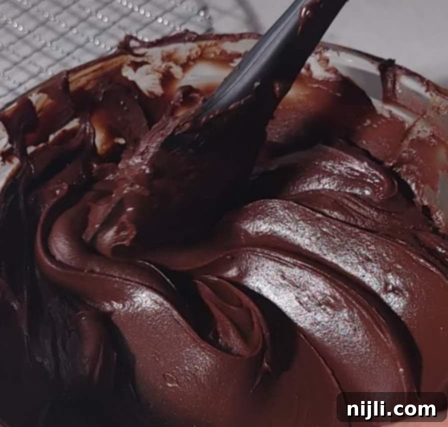 Rich Chocolate Fudge Frosting 5 A spatula mixing thick chocolate fudge frosting in a bowl, illustrating the creamy consistency ideal for chocolate fudge frosting preparation.