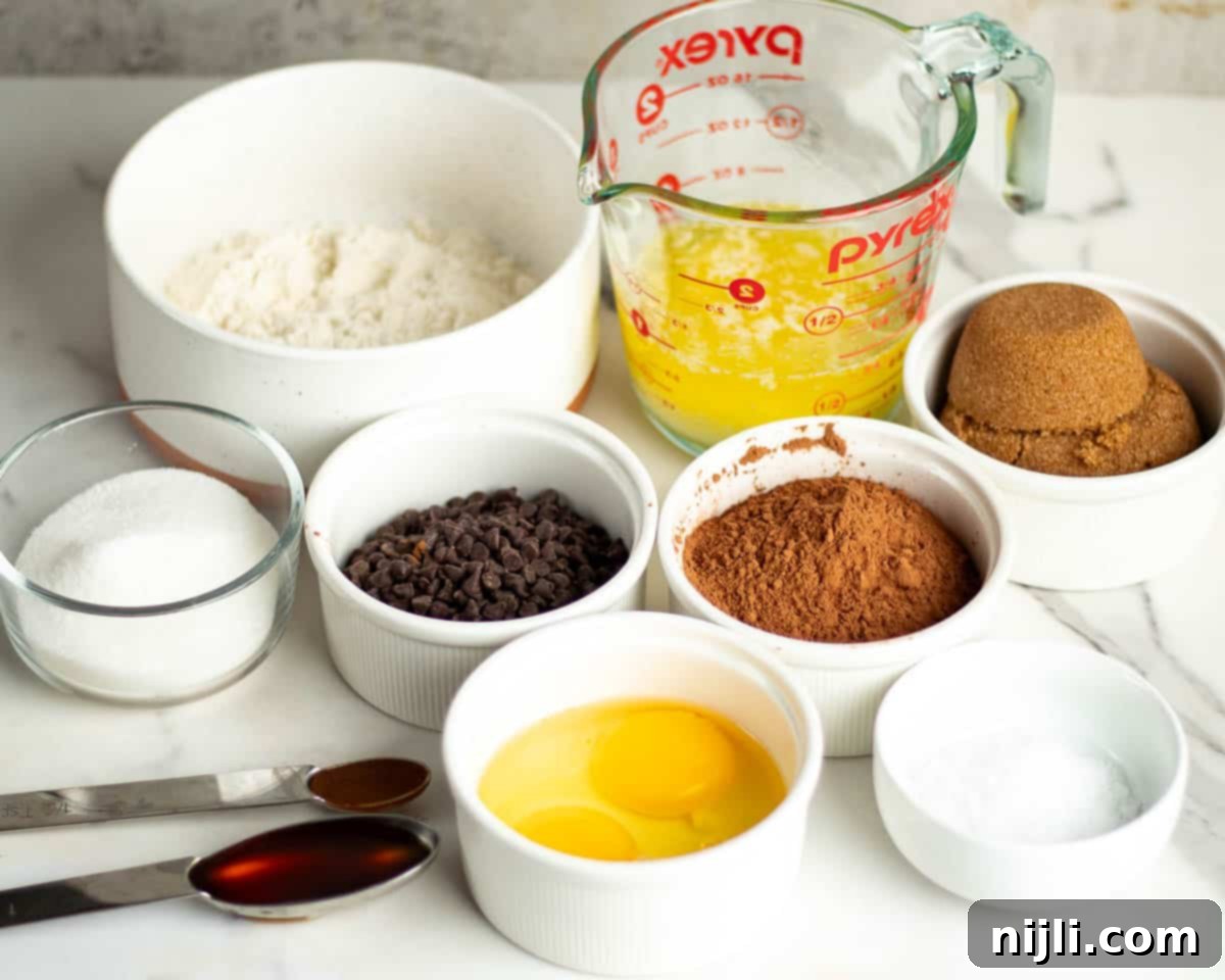 Bite-Sized Brownies 5 Various ingredients for making 2 bite brownies arranged on a white countertop, including flour, sugar, chocolate chips, cocoa powder, eggs, brown sugar, melted butter, vanilla extract, and salt.