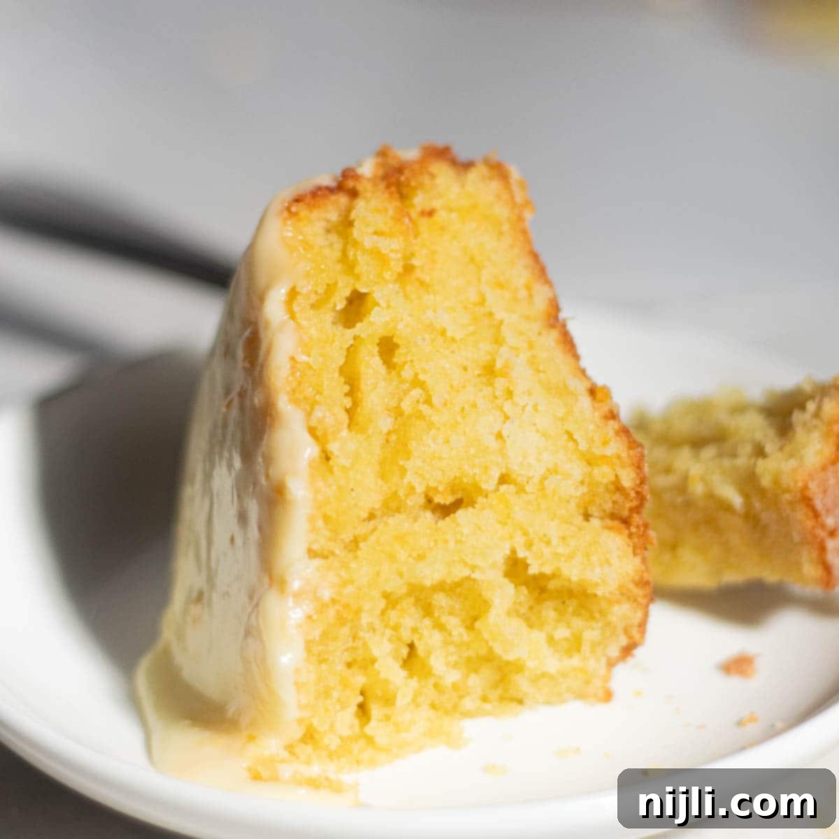 Mediterranean Gluten-Free Olive Oil Cake 6 Close-up of a slice of gluten-free olive oil cake drizzled with a rich, creamy orange glaze, emphasizing its golden, tender crumb and moist texture.