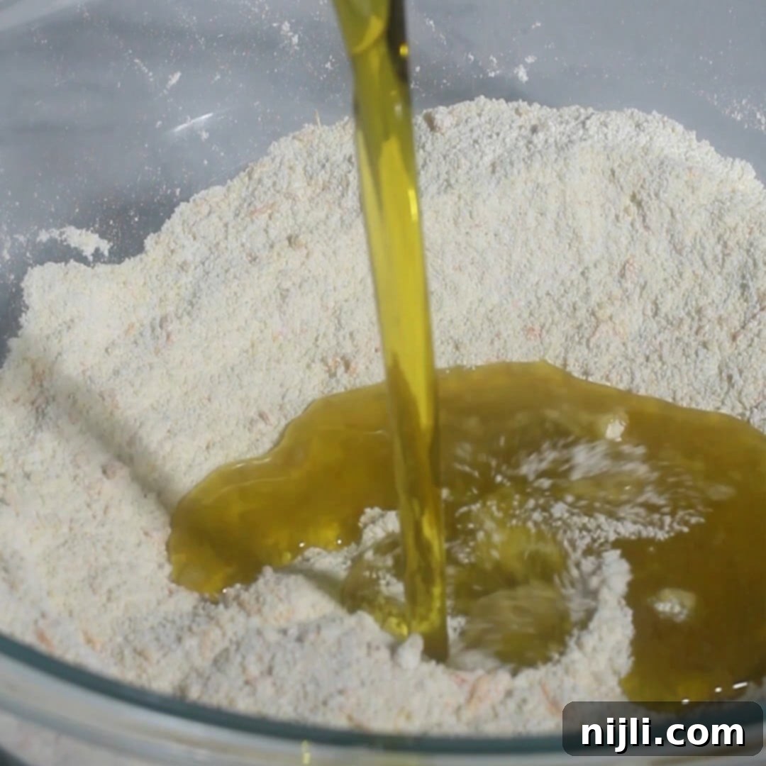 Mediterranean Gluten-Free Olive Oil Cake 9 Pouring extra-virgin olive oil into the dry ingredients for a gluten-free olive oil cake, followed by mixing in room-temperature eggs one at a time.