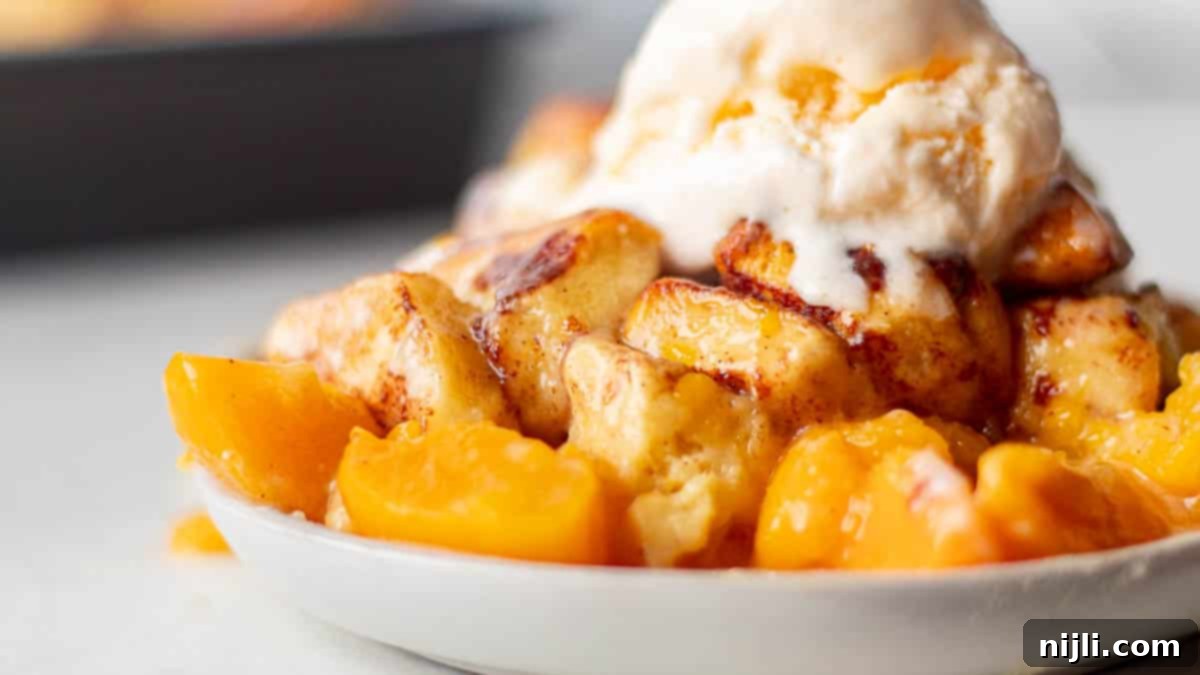 A close-up of cinnamon rolls peach cobbler made with canned peaches, highlighting the peach slices and cinnamon swirl rolls.