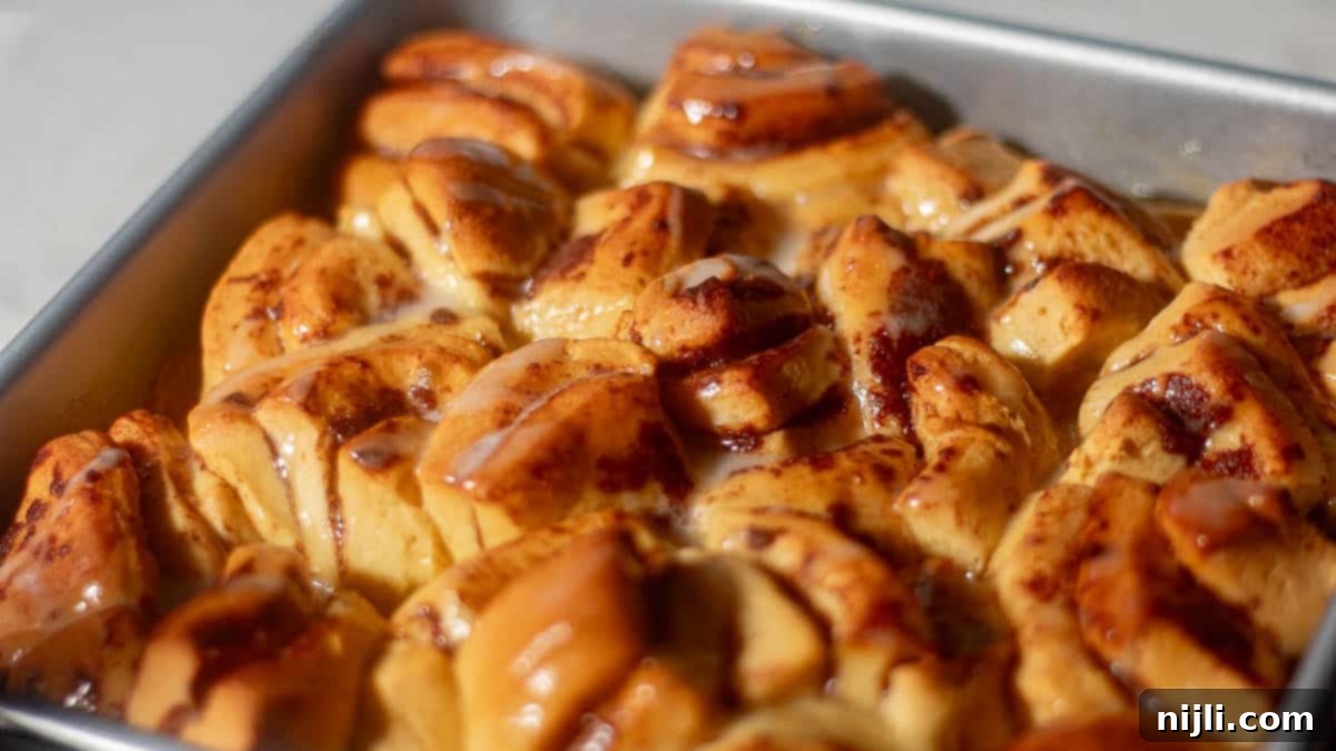 Close-up image of a freshly baked cinnamon rolls peach cobbler in a baking pan. The cobbler features golden-brown cinnamon rolls with a drizzle of icing on top, showcasing a glossy and delicious finish.