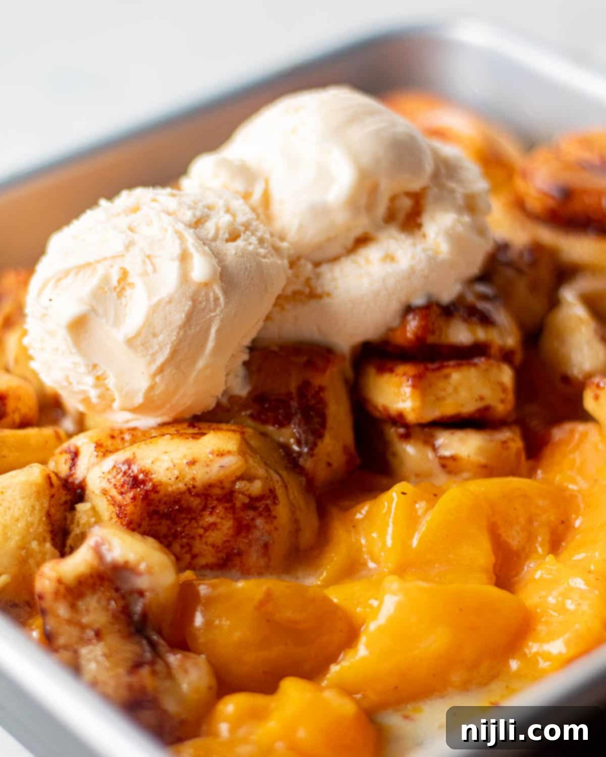 An old fashioned cinnamon rolls peach cobbler in a baking pan, featuring a crispy, golden brown top and juicy peaches underneath.