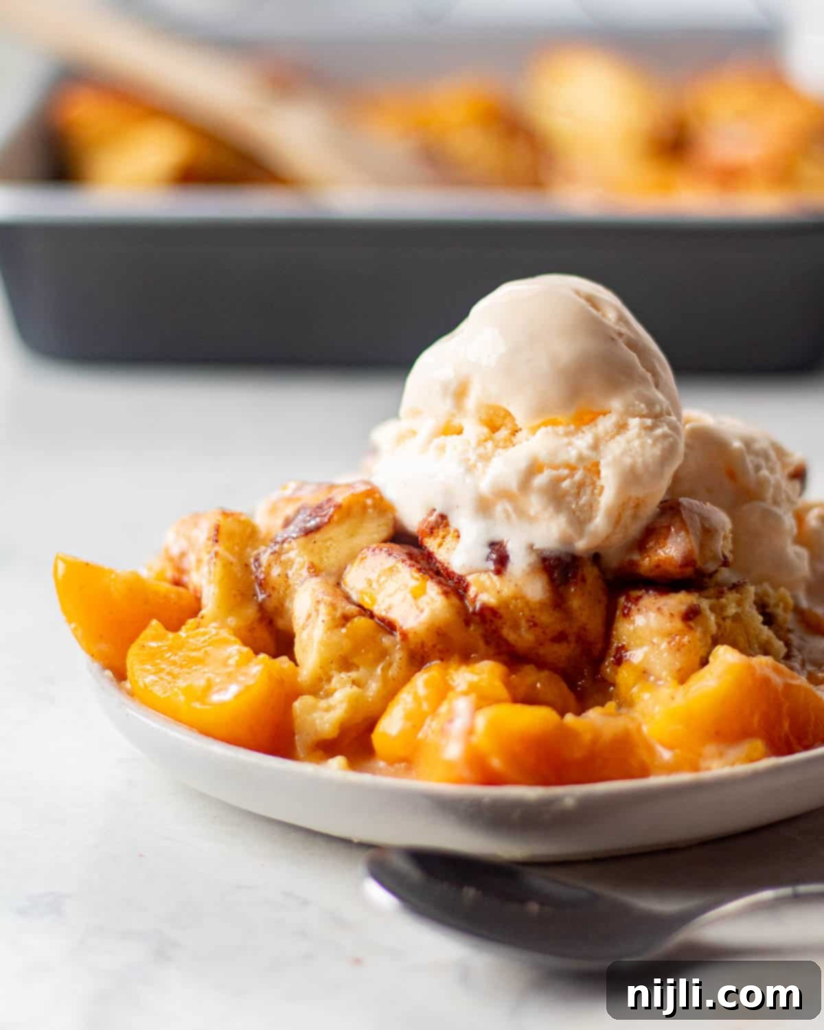 Image of a dessert plate featuring cinnamon rolls peach cobbler topped with a scoop of vanilla ice cream. 