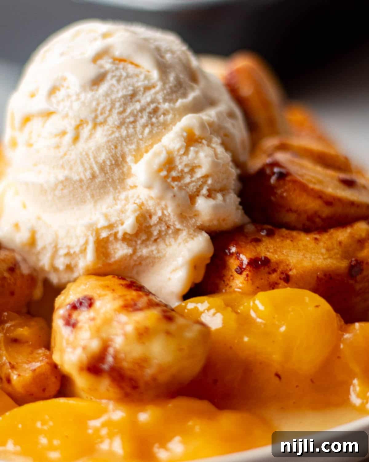 A detailed shot of cinnamon rolls peach cobbler, topped with melting vanilla ice cream and surrounded by tender peach slices.