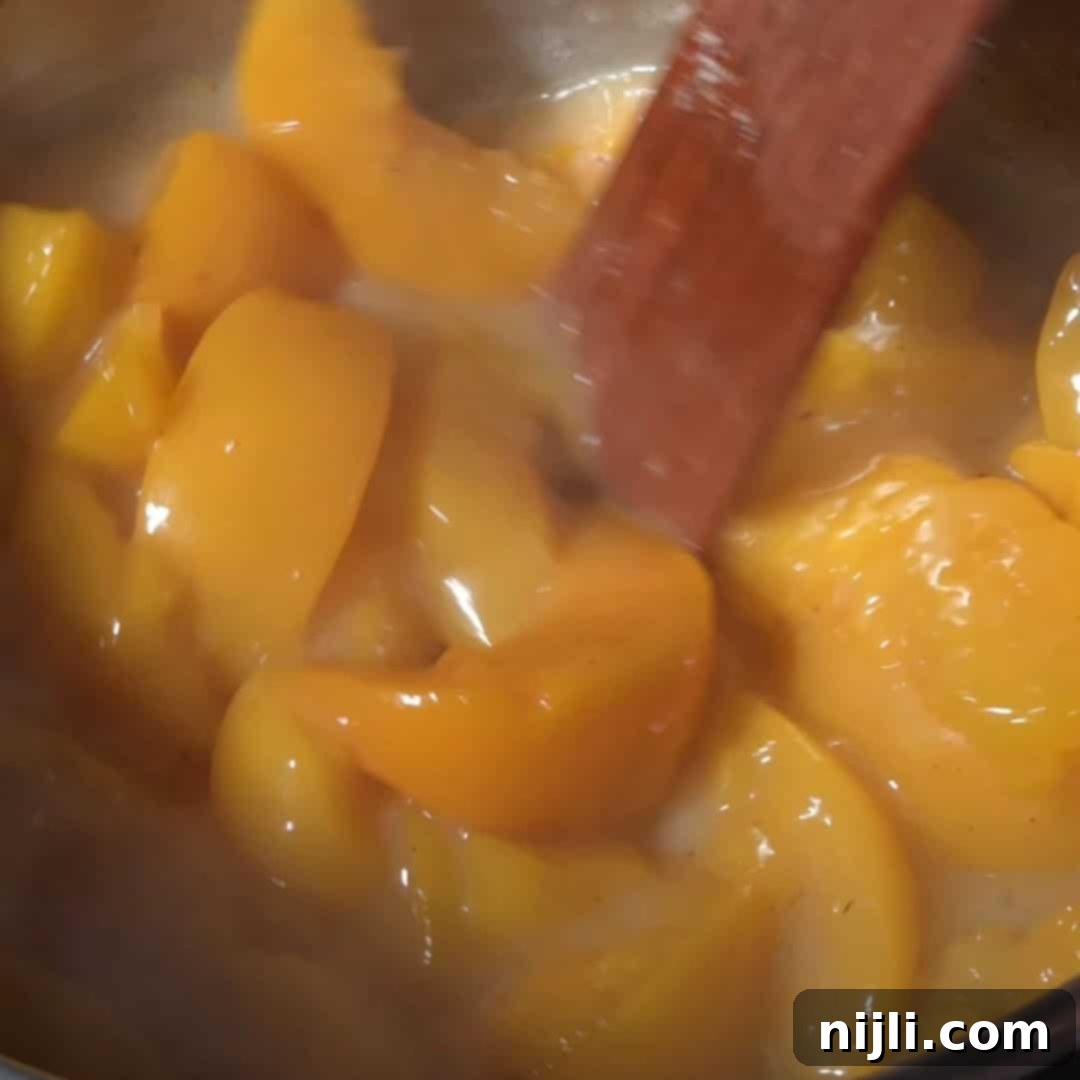 A pot of simmering peach slices being stirred, preparing the peach filling for cinnamon rolls peach cobbler.