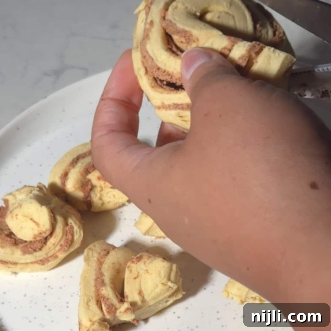 A person holding a cut cinnamon roll dough piece above a plate, ready to place it on the peaches for the cinnamon rolls peach cobbler.