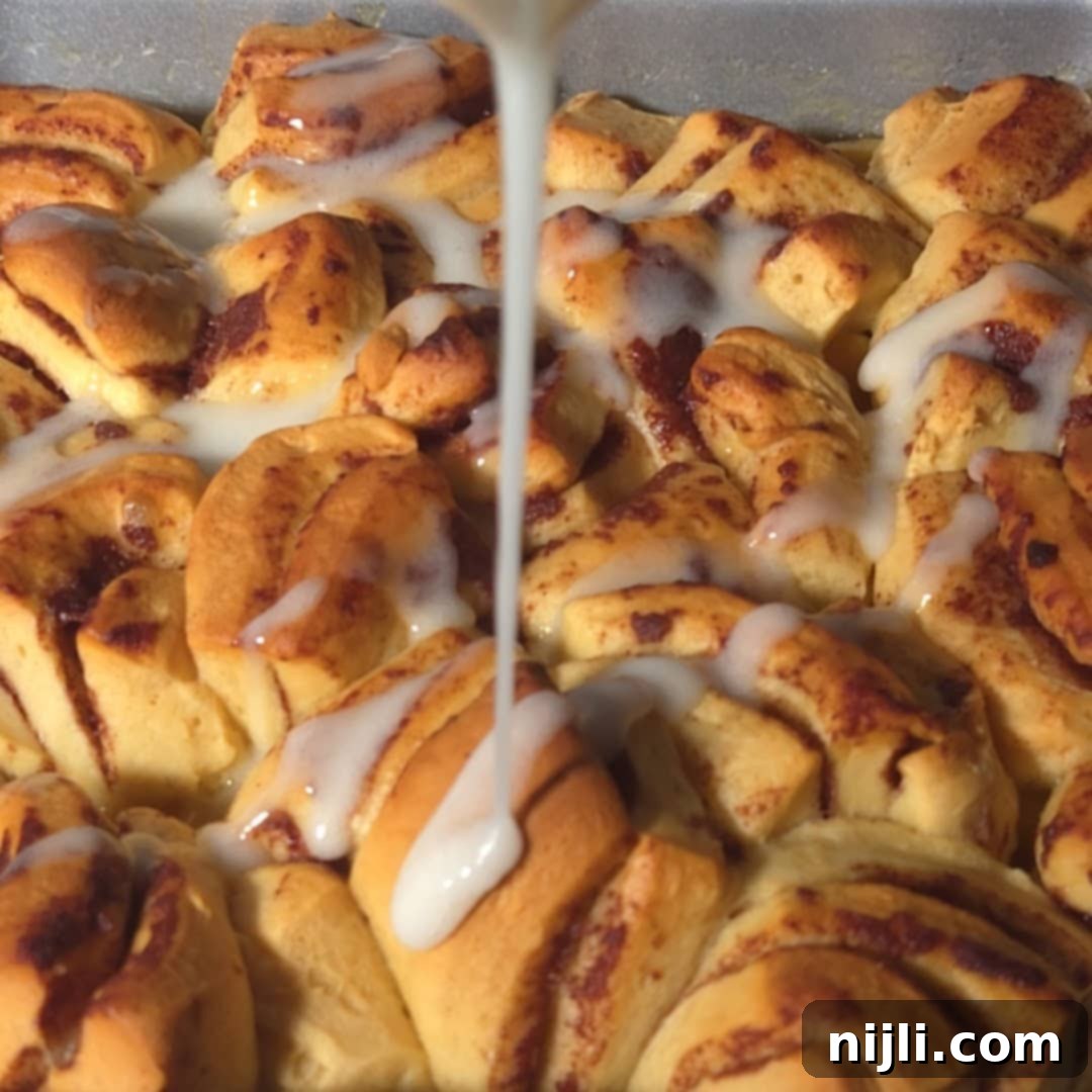A close-up of icing being drizzled over freshly baked cinnamon rolls peach cobbler, highlighting the golden brown rolls and sweet glaze.