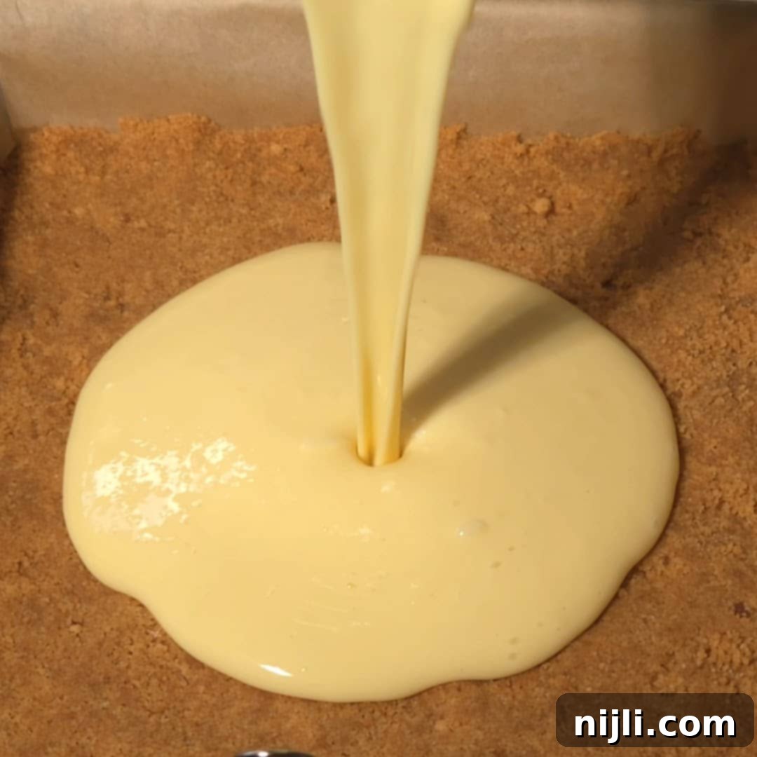 Golden Lemon Delight with Graham Crumb Perfection 11 Creamy lemon filling being poured onto a graham cracker crust in a baking dish, highlighting the process of making lemon bars with graham cracker crust.