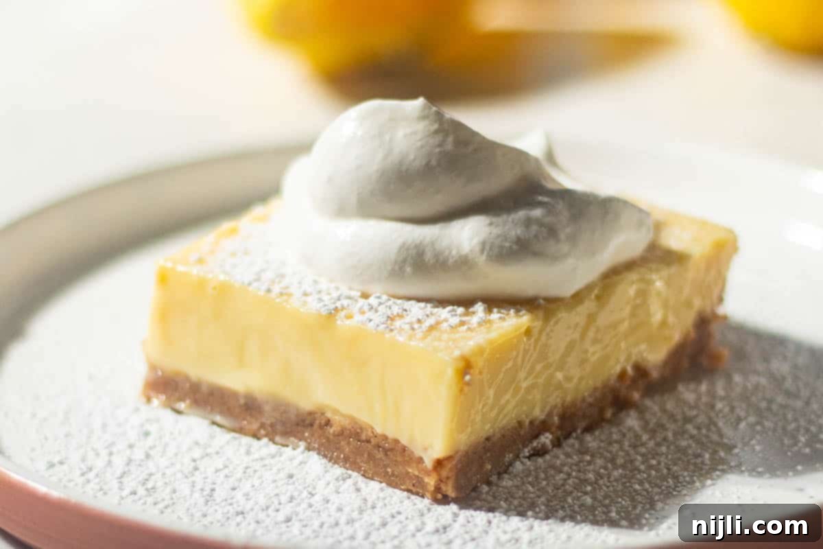 Golden Lemon Delight with Graham Crumb Perfection 14 A lemon bar with a graham cracker crust and a generous layer of whipped cream on top, dusted with powdered sugar, with bright yellow lemons in the background.