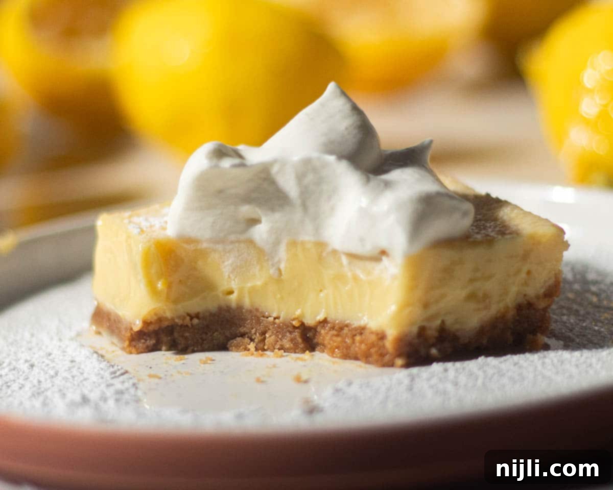 Golden Lemon Delight with Graham Crumb Perfection 6 A partially eaten lemon bar with a graham cracker crust and whipped cream on top, revealing the creamy lemon filling, with lemons blurred in the background.