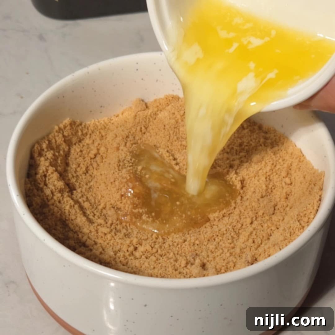 Golden Lemon Delight with Graham Crumb Perfection 8 Melted butter being poured into a bowl of graham cracker crumbs to create the crust for lemon bars, with a smooth and consistent mixture being formed.