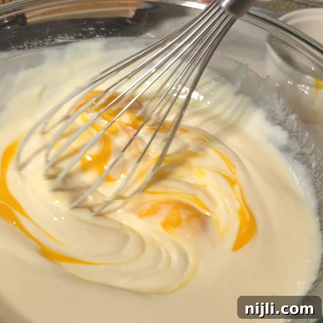 Golden Lemon Delight with Graham Crumb Perfection 10 A whisk blending egg yolks into a creamy lemon mixture in a glass bowl, part of the preparation process for lemon bars with graham cracker crust.