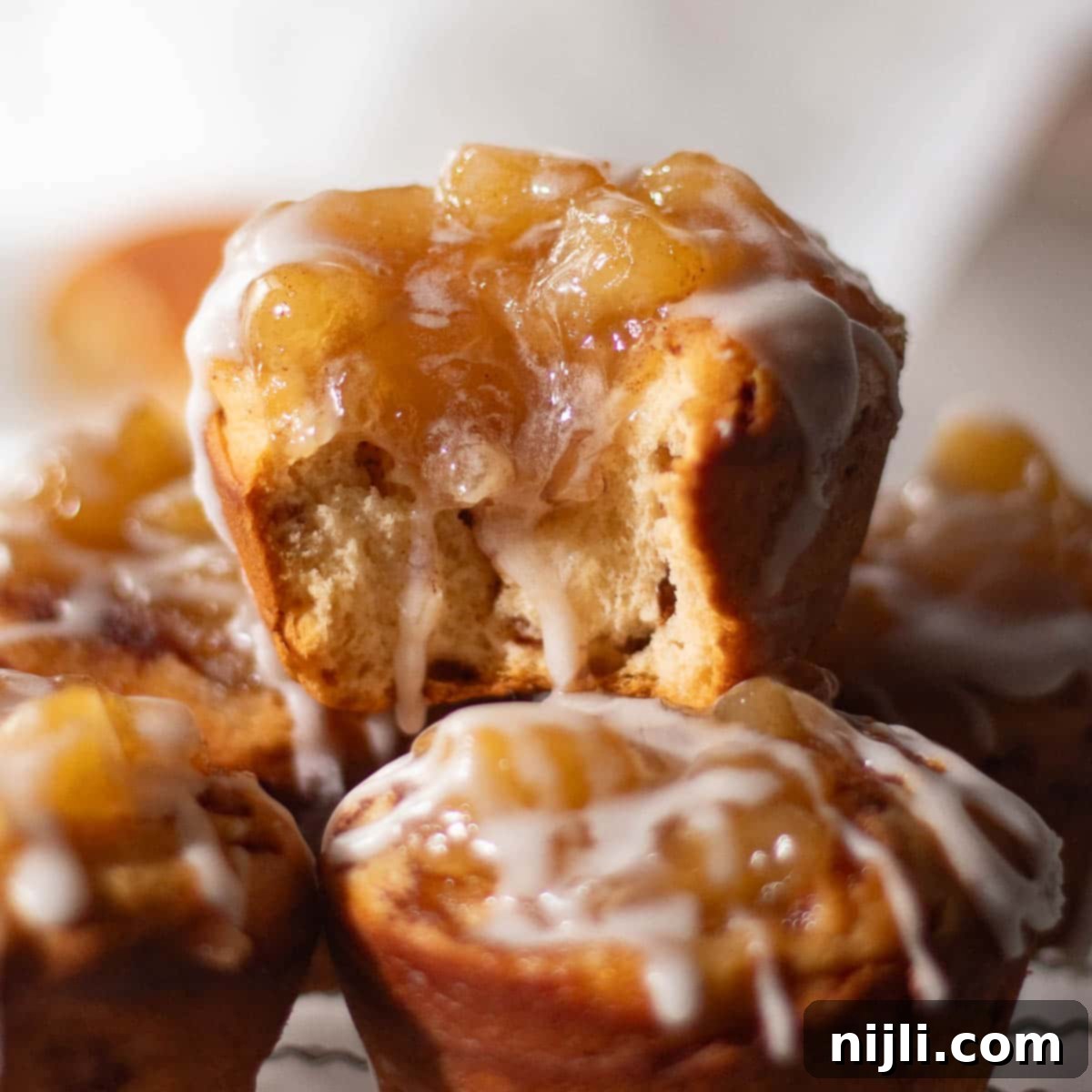 Cinnamon Swirl Apple Pies 12 Freshly baked cinnamon roll apple pies on a cooling rack, topped with warm apple pie filling and a drizzle of sweet icing, showcasing the perfect fall dessert.