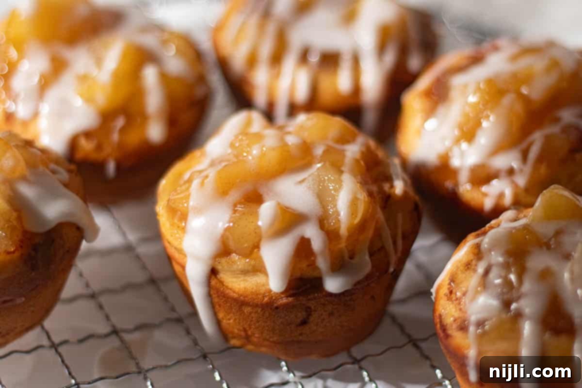 Cinnamon Swirl Apple Pies 5 Baked cinnamon roll apple pies featuring fresh apple pieces, topped with icing, sitting on a cooling rack.