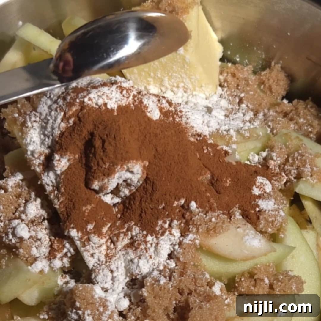 Effortless Cake Mix Apple Cobbler 7 Cinnamon and sugar being added to sliced apples in a pan, preparing the filling for apple cobbler with yellow cake mix.