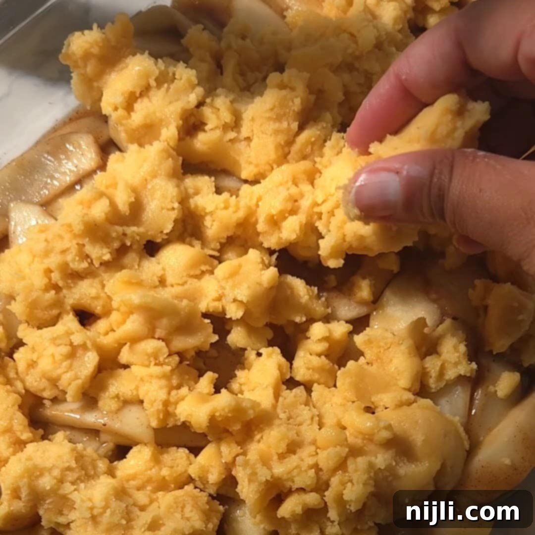 Effortless Cake Mix Apple Cobbler 10 Hand sprinkling yellow cake mix over a layer of sliced apples in a baking dish, a step in preparing apple cobbler with yellow cake mix.