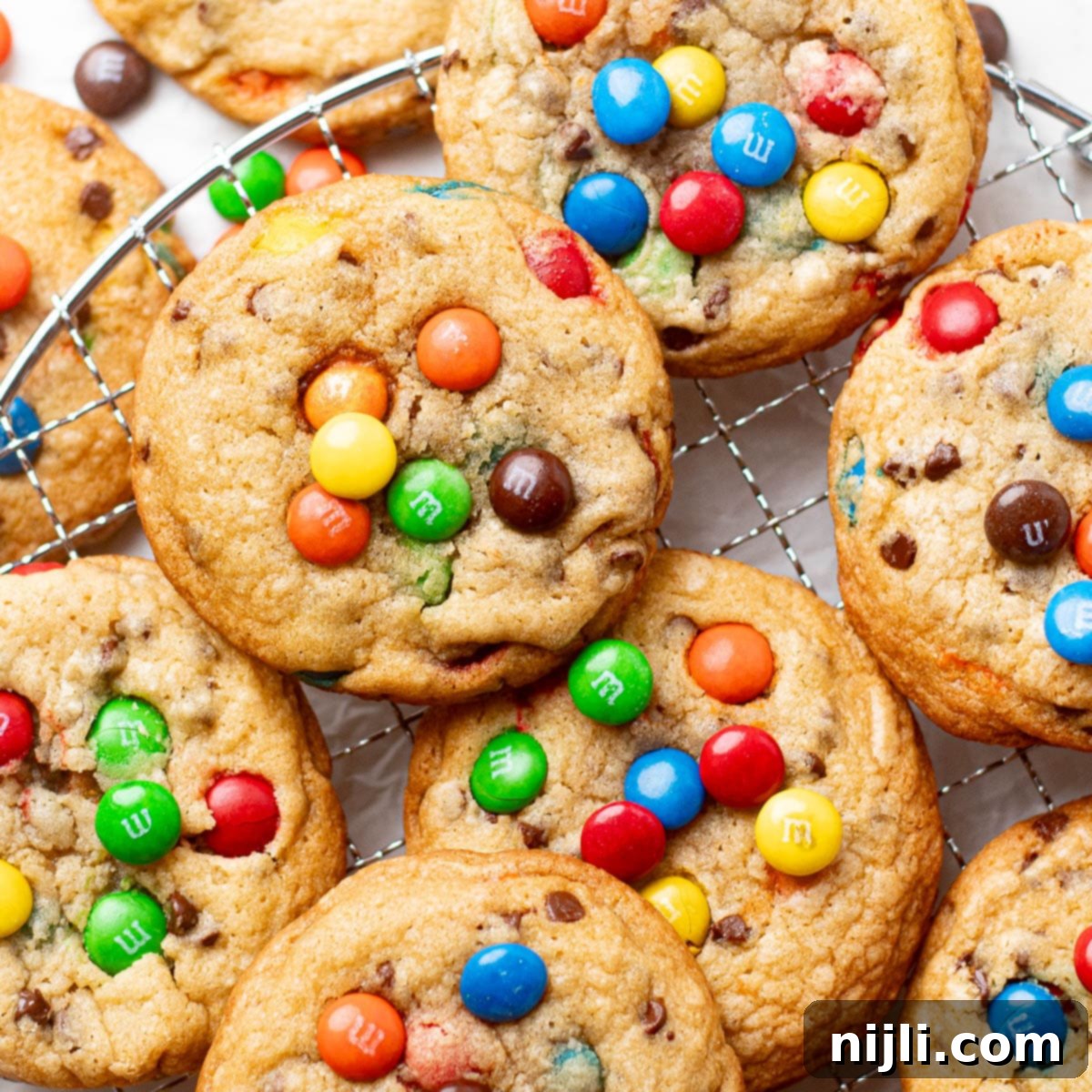 M&M Burst Chocolate Chip Goodness 2 A stack of chocolate chip M&M cookies showcasing a mix of gooey chocolate chips and colorful M&M candies in a thick, golden cookie dough. These cookies capture the perfect balance of chocolate and candy, making them ideal for anyone craving a fun twist on traditional chocolate chip cookies.