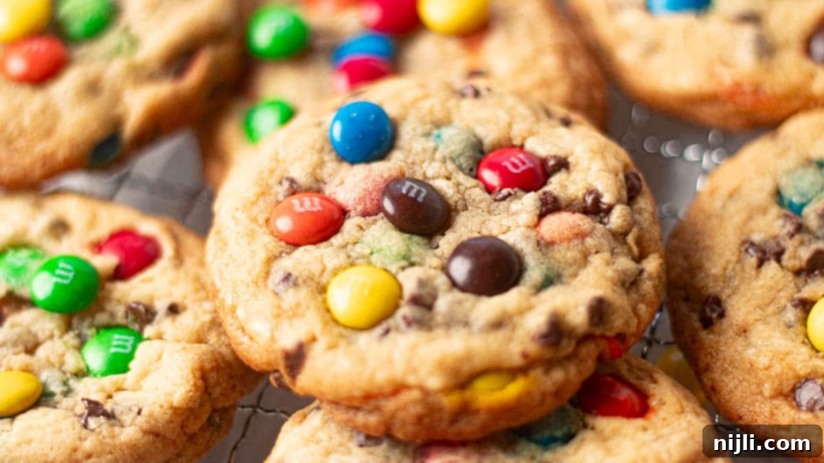 M&M Burst Chocolate Chip Goodness 4 A close-up of freshly baked M&M cookies piled on a cooling rack, each cookie packed with colorful candy-coated chocolates in a golden, chewy dough. These cookies exemplify the classic M&M cookies recipe, offering a vibrant and delicious treat that's both chewy and crisp around the edges.