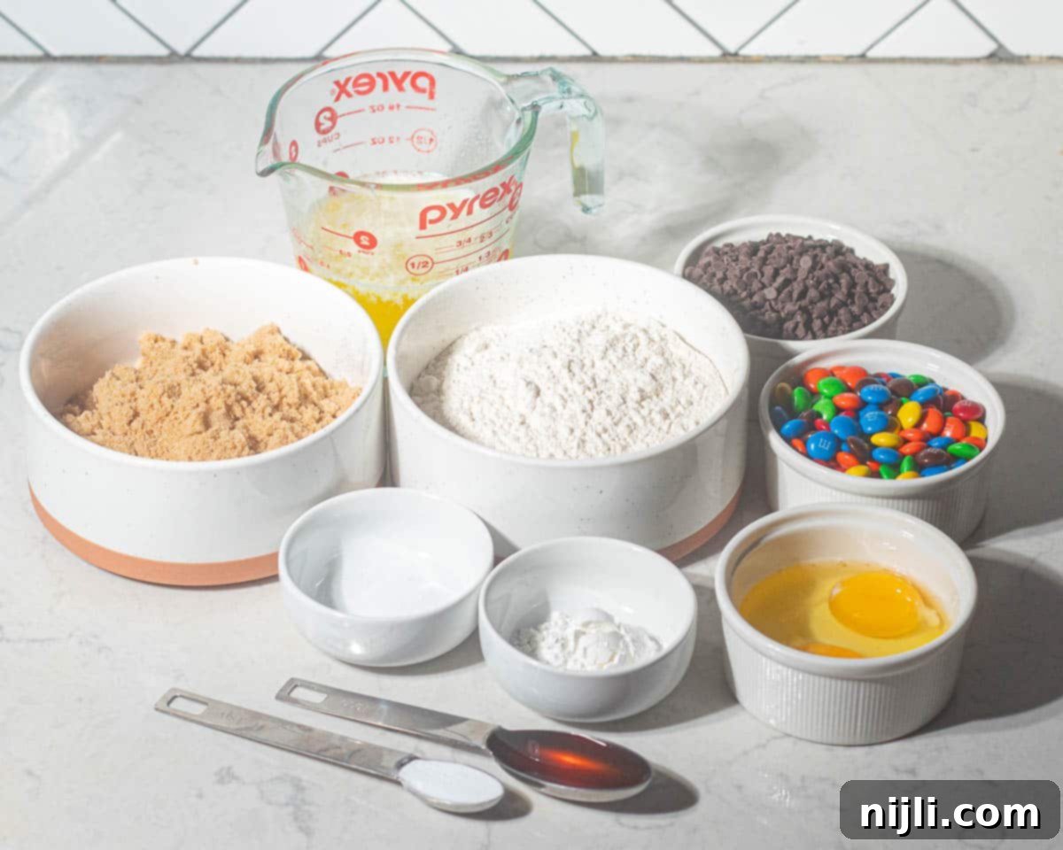 M&M Burst Chocolate Chip Goodness 5 A flat lay of ingredients for chocolate chip cookies with M&Ms, including flour, brown sugar, mini chocolate chips, and vibrant M&M candies. This image offers a visual guide for assembling everything needed to make chewy, colorful M&M chocolate chip cookies from scratch.