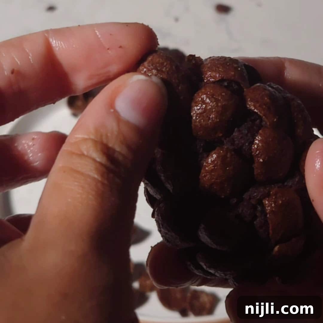 Delicious Pinecone Brownie Recipe 8 A close-up of hands carefully pressing chocolate cereal pieces into a brownie base to create the layered pinecone effect. The details of the process are clearly visible.