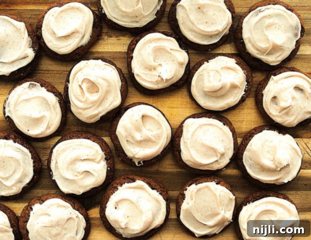 Stout-Infused No-Chill Gingerbread Cookies with Brown Butter Cream Cheese Frosting 2 Overhead view of several no-chill gingerbread molasses cookies, some frosted with white cream cheese frosting and some plain, arranged on a cooling rack, showcasing their soft texture and rich, dark color.
