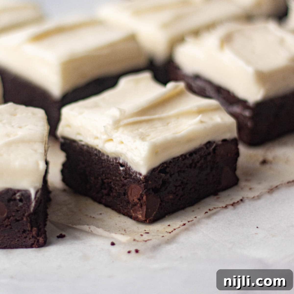 Angled view of sliced brownies with cream cheese frosting, highlighting the contrast between the rich chocolate base and the smooth, creamy topping. The dessert is perfect for chocolate lovers.