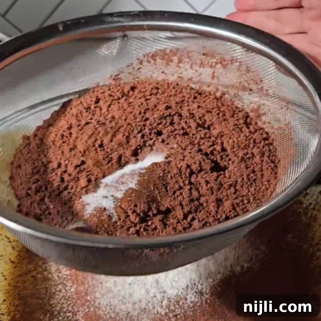 Cocoa powder and dry ingredients being sifted into a mixing bowl, a key step in preparing the batter for brownies with cream cheese frosting. This process ensures smooth and lump-free brownies.