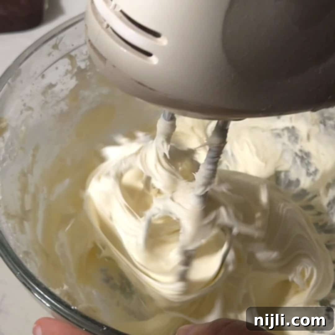 A handheld electric mixer blending cream cheese frosting to a fluffy consistency, perfect for topping brownies.
