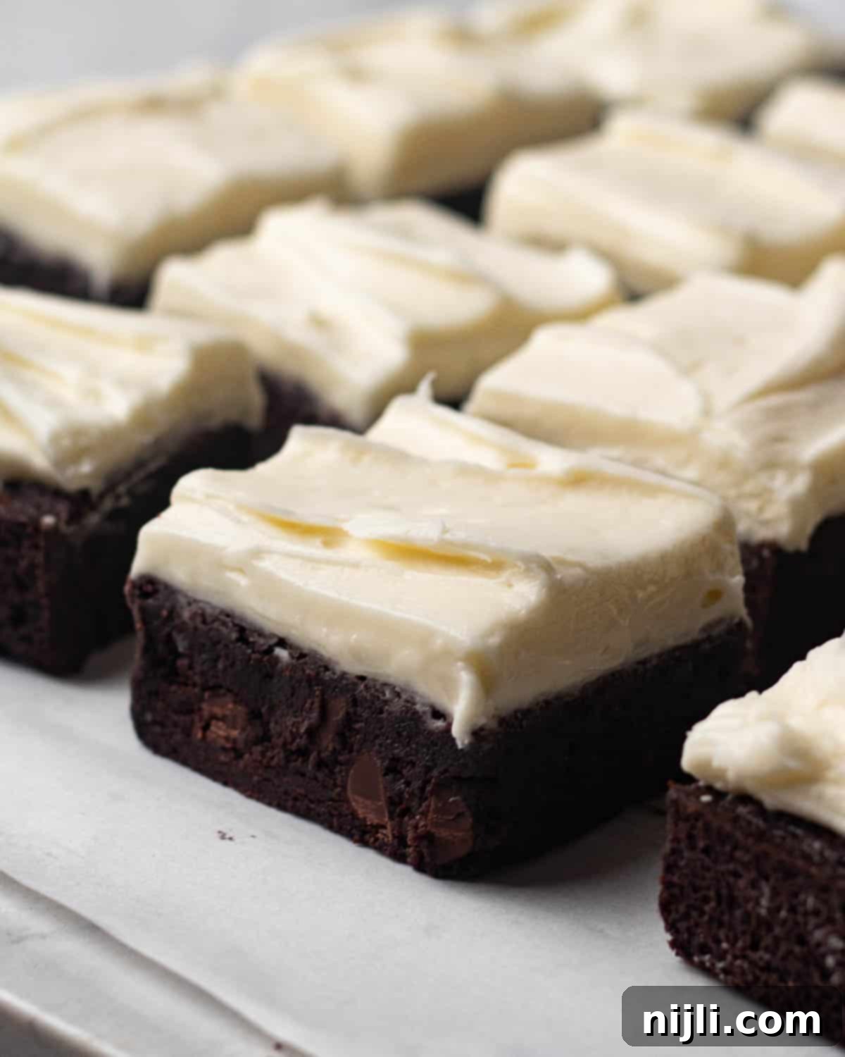 Angled view of brownies with cream cheese frosting, showcasing the fudgy chocolate base and creamy topping. These decadent treats are sliced and ready to serve, ideal for any occasion.