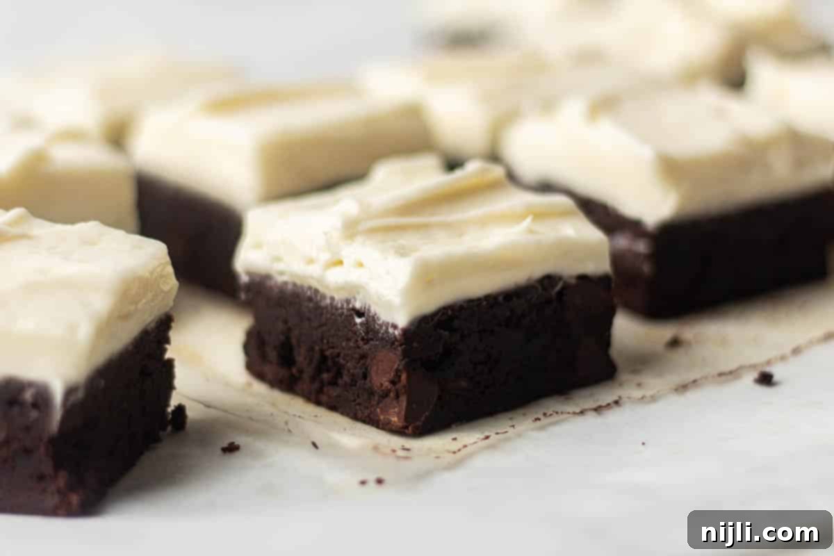 Angled view of brownies with cream cheese frosting, showcasing the fudgy chocolate base and creamy topping. These decadent treats are sliced and ready to serve, ideal for any occasion.