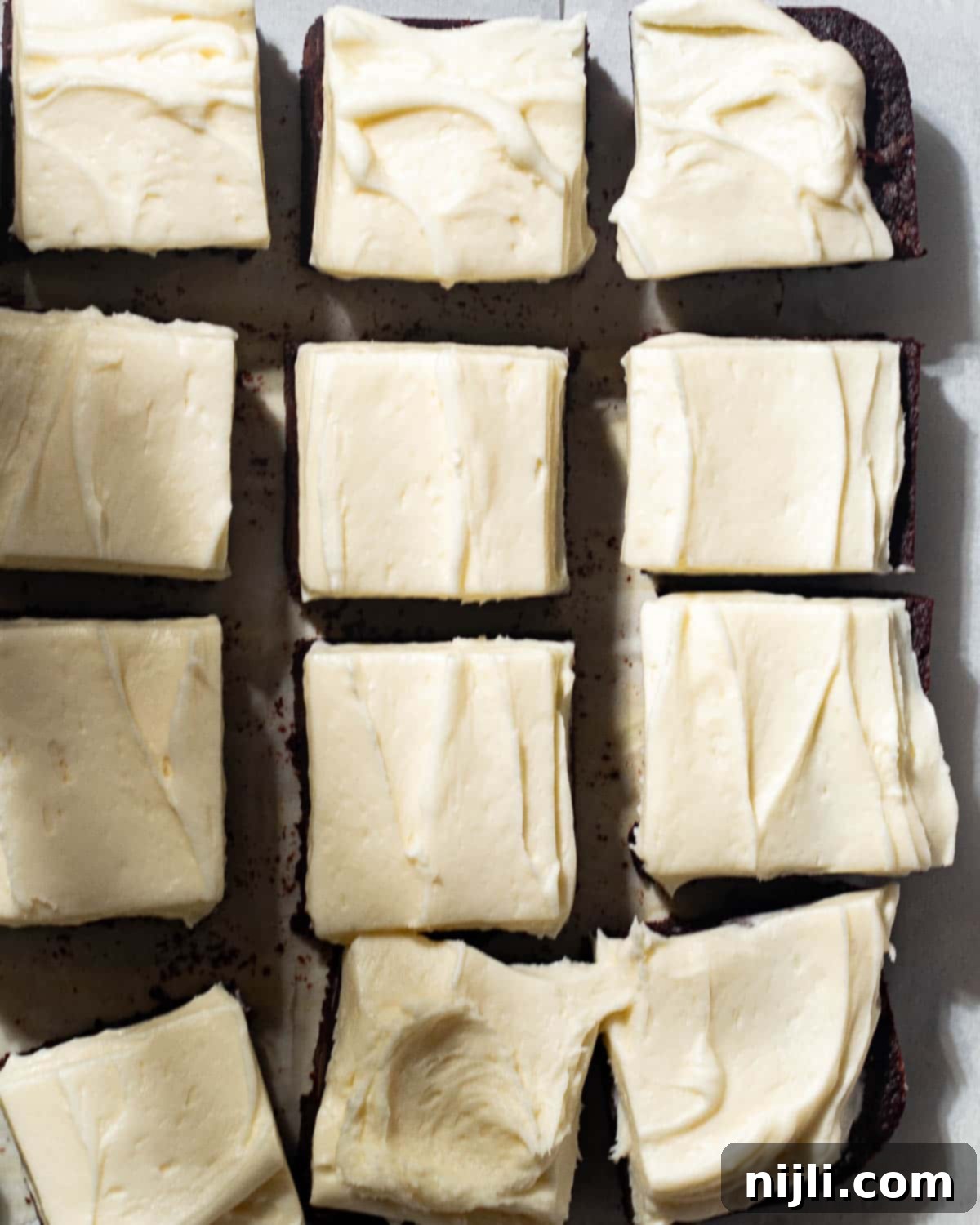 Overhead view of a batch of brownies topped with thick cream cheese frosting, sliced into even squares. The rich chocolate base and smooth frosting create a perfect dessert for brownie lovers.