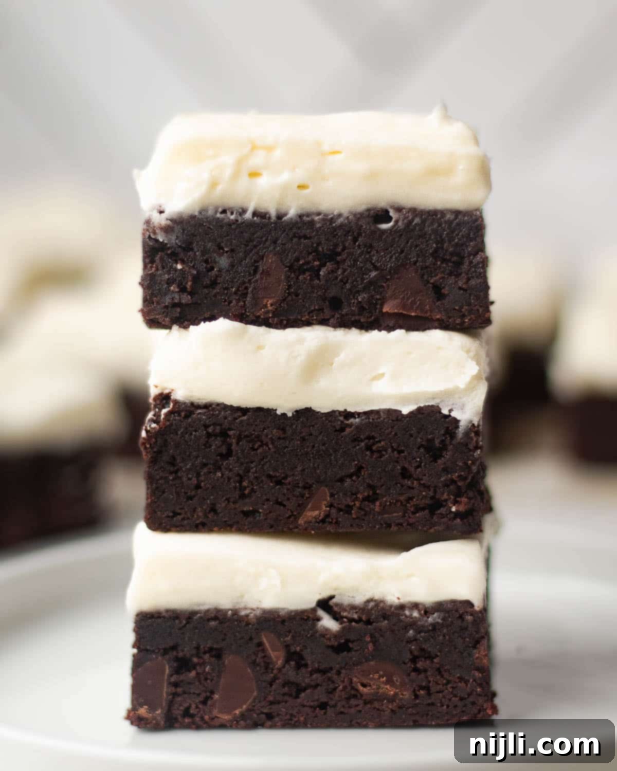 A close-up stack of brownies with cream cheese frosting, highlighting the thick, creamy layer of frosting and chocolate chunks in the fudgy base. Perfect for showcasing the ultimate dessert idea.