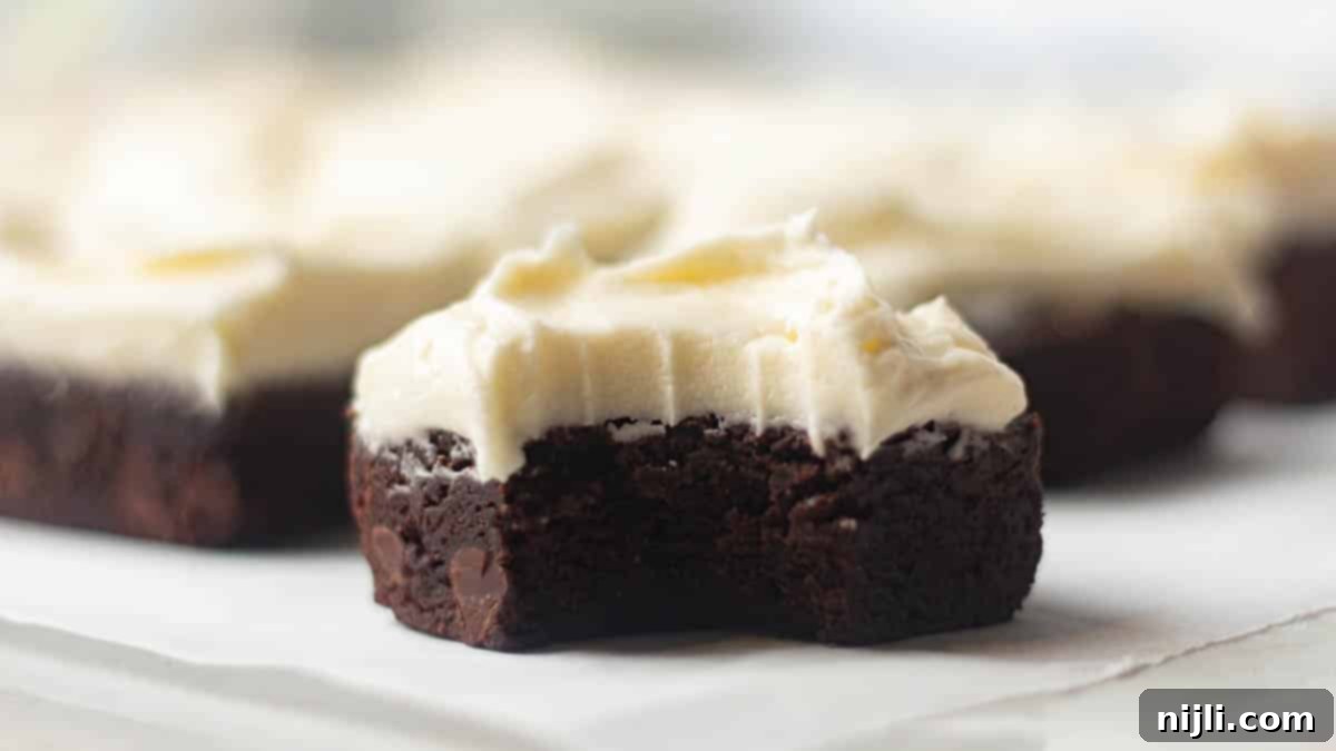 A partially eaten brownie topped with cream cheese frosting, revealing its moist, chocolatey center.