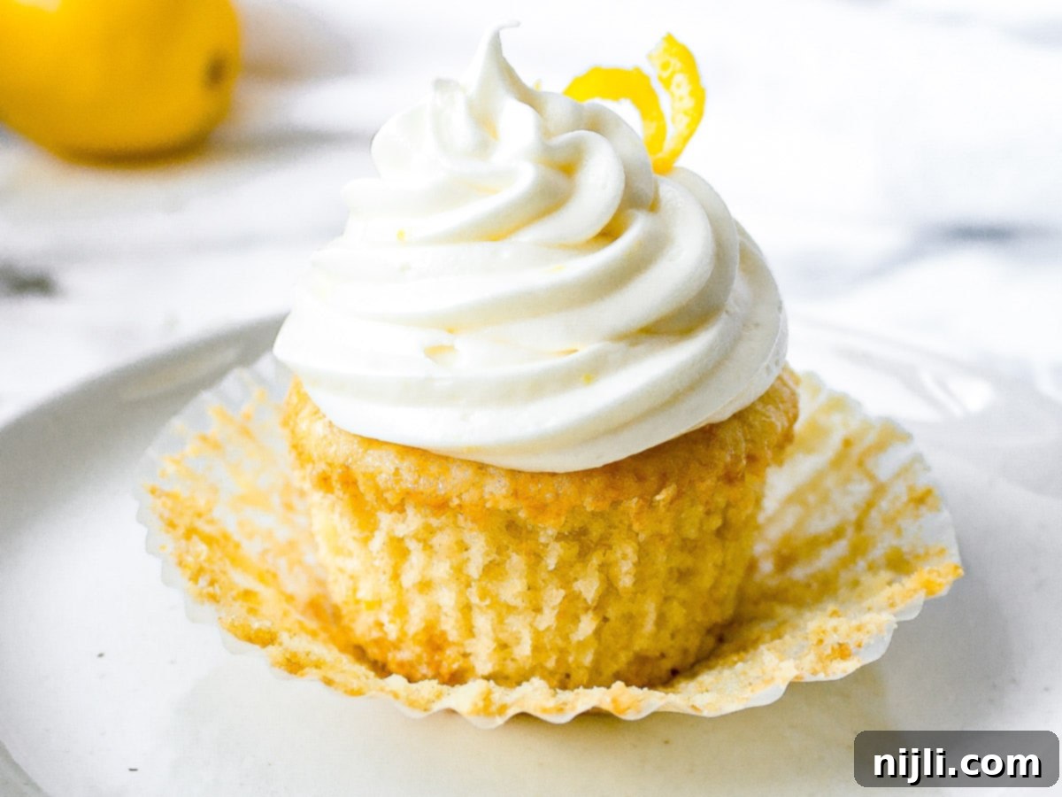 Aromatic Lavender Lemon Cupcakes 3 A single lavender lemon cupcake with its wrapper peeled back, revealing its soft, moist texture and topped with a swirl of lemon cream cheese frosting and a sprinkle of lemon zest.