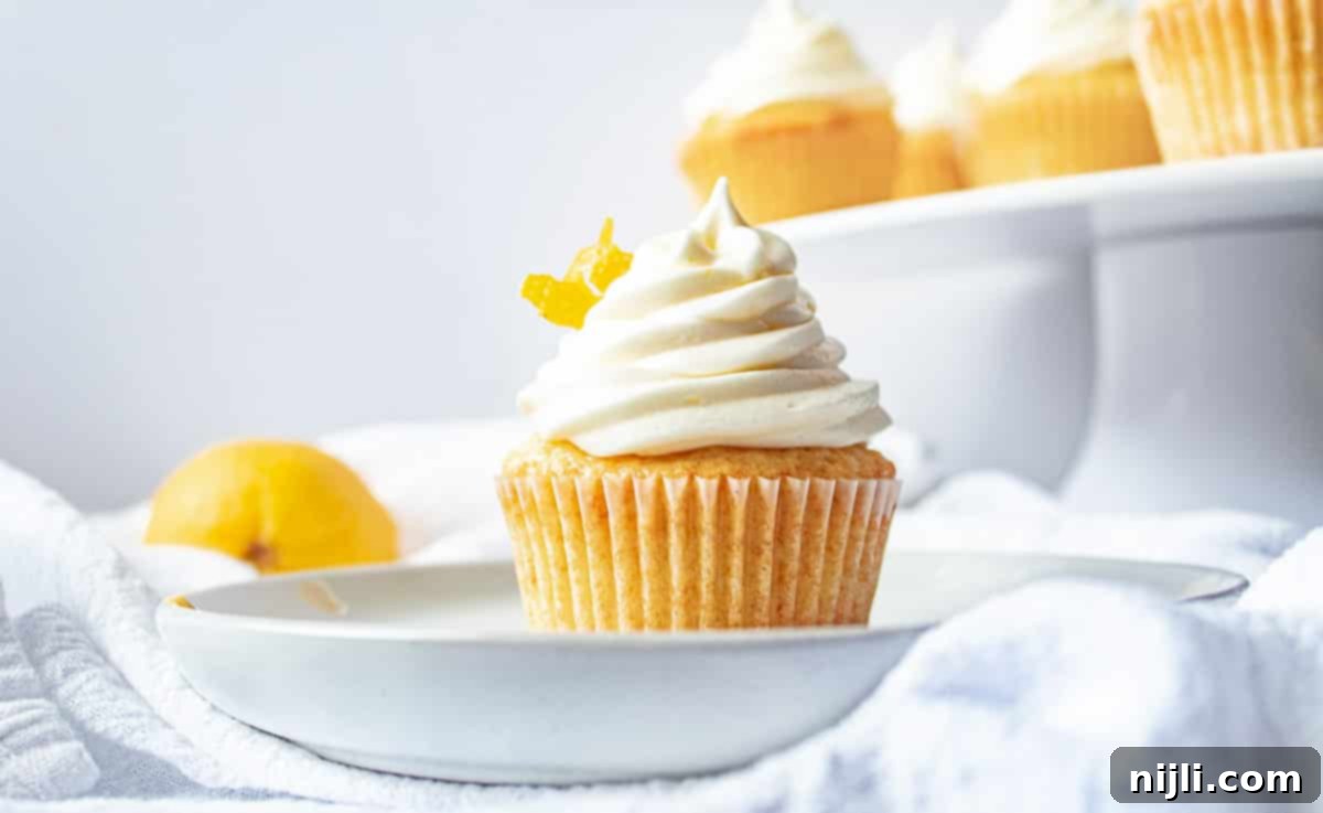 Two lavender lemon cupcakes on a plate, with a background tray of more cupcakes, showcasing the creamy frosting texture.