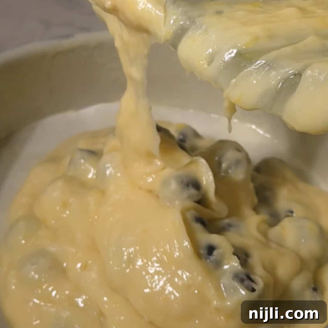 Sunny Lemon Blueberry Mascarpone Delight 11 Batter with fresh blueberries being poured into a parchment-lined cake pan, ready to bake into a lemon blueberry mascarpone cake.
