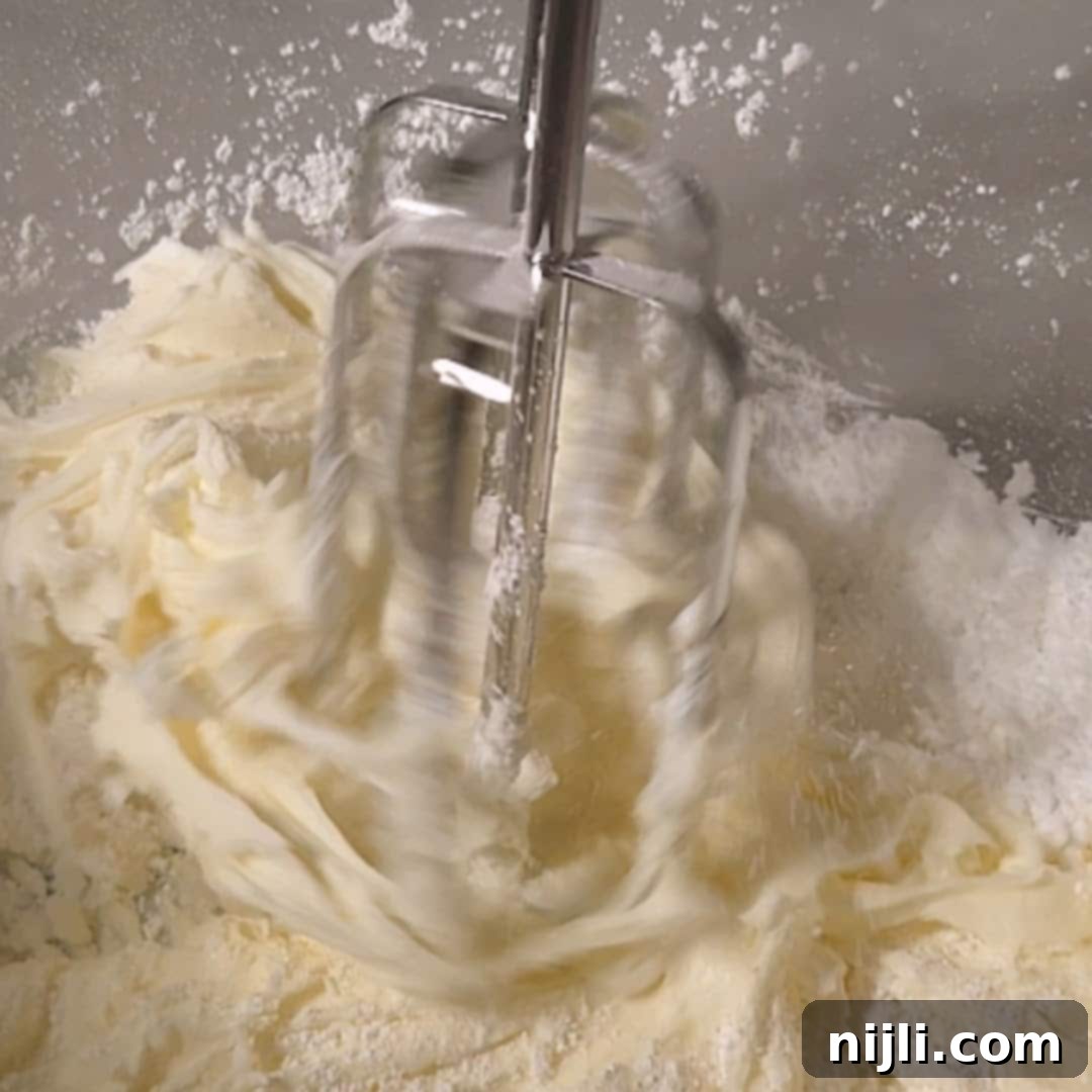 Sunny Lemon Blueberry Mascarpone Delight 12 Electric mixer blending mascarpone cheese and powdered sugar in a glass bowl, forming the smooth whipped topping for a lemon blueberry mascarpone cake.