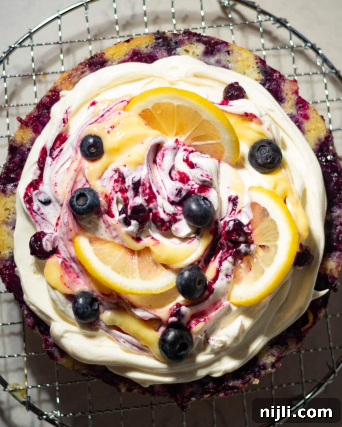 Sunny Lemon Blueberry Mascarpone Delight 15 Whole lemon blueberry mascarpone cake on a cooling rack, topped with mascarpone cream, lemon curd, blueberry compote, and lemon slices, ready to serve.