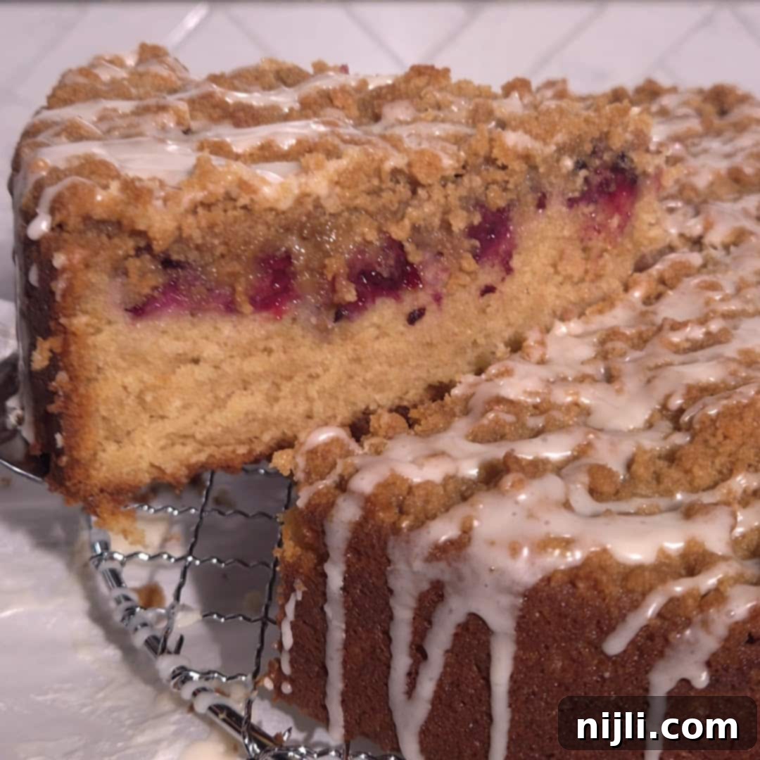 Homemade Blackberry Coffee Cake 14 A slice of blackberry coffee cake is lifted from the whole, showcasing a moist vanilla crumb, rich blackberry filling, and golden streusel topping with vanilla glaze.