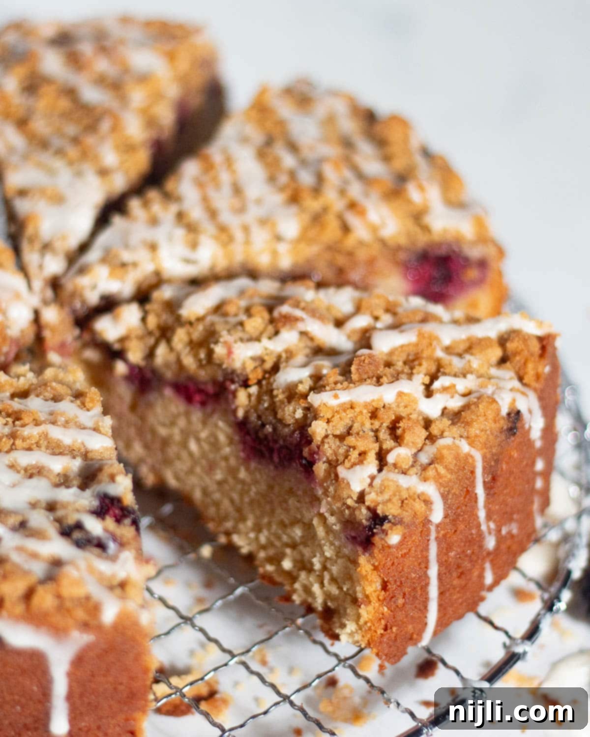 Homemade Blackberry Coffee Cake 15 A full blackberry coffee cake with one slice removed, sitting on a wire rack. The inside reveals a thick golden crumb and a rich blackberry swirl beneath a crunchy streusel topping.