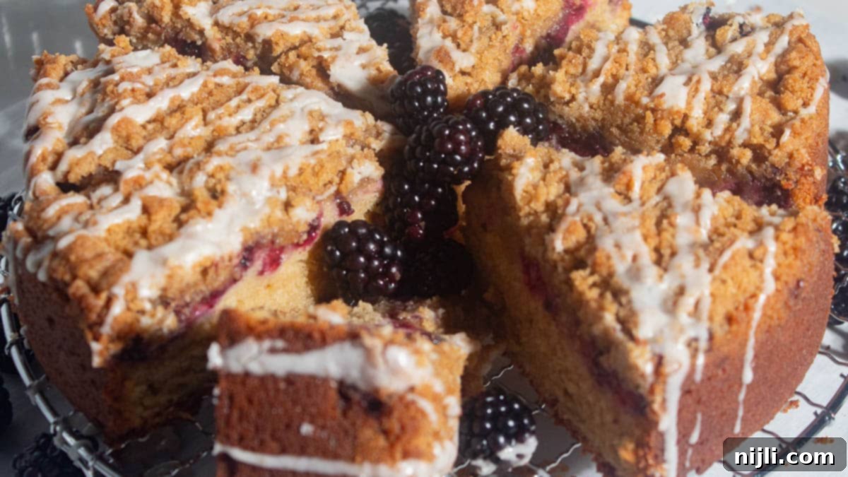Homemade Blackberry Coffee Cake 3 Overhead shot of a whole blackberry coffee cake sliced into wedges and arranged with fresh blackberries in the center. Vanilla glaze is drizzled over the golden crumb topping.